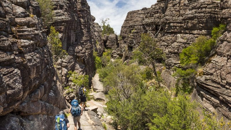 Adventurers hiking through a scenic rocky gorge on the Great Ocean Road Grampians Overnight Escape from Melbourne beneath clear blue skies.