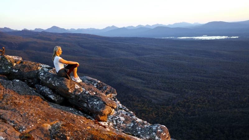 Woman on rugged cliff edge, gazing at scenic coast, envisioning a 3 Day Great Ocean Road Grampians Explorer tour from Melbourne.