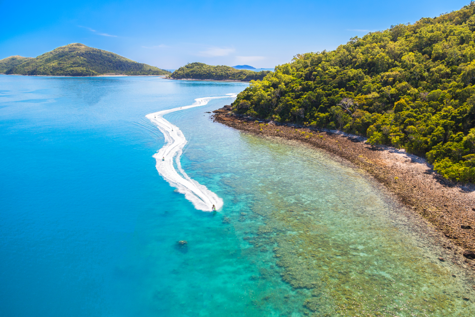 A speedboat creates a foamy white wake near vibrant green islands during the Two Island Safari 2 Hour Jetski Tour adventure.