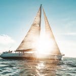 Experience the Broomstick 2 Day 2 Night Whitsunday Sailing boat gliding at sunset, golden sunlight streaming through sleek white sails.