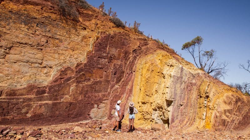 Two travellers hike among striking layered rock formations on a 4-day Uluru, Kata Tjuta, Kings Canyon, and West MacDonnell tour.