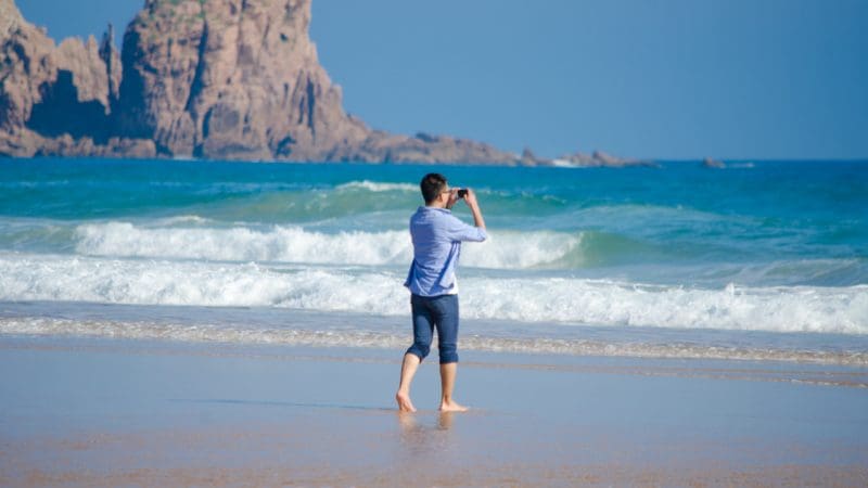 Barefoot visitor enjoys panoramic sea views at Phillip Island Penguin Parade as playful koalas wander nearby on the sandy beach.