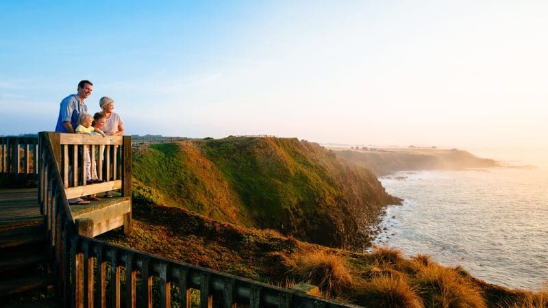 Family overlooks scenic ocean views from lush Phillip Island cliffs at sunset during Penguin Parade and Koala tour adventure.