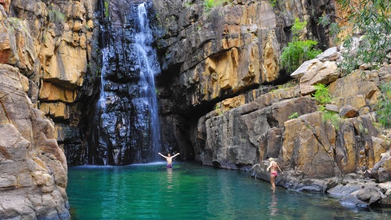 Adventurers swimming and exploring by the stunning Edith Falls waterfall on a Katherine Gorge day cruise experience from Darwin, Australia.