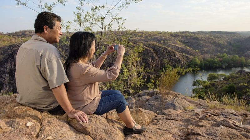 A couple sits on rugged rocks, photographing the breathtaking canyon views on their 4-day Kakadu Katherine Gorge adventure tour.