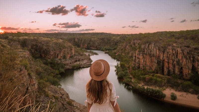 Woman in hat gazes over scenic river winding through dramatic rocky cliffs on 5 Day Kakadu Katherine Gorge Adventure tour, Australia.