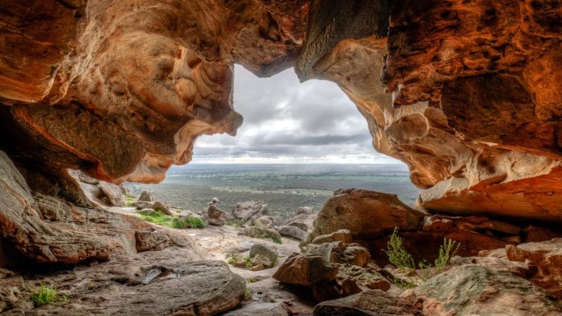 Stunning view from inside a rocky cave on the 3 Day Great Ocean Road Grampians Explorer, under dramatic cloudy Melbourne skies.