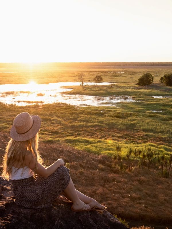 Woman in hat sits on rock, gazing at sunset during 3 Day Kakadu Litchfield National Park 4WD Safari Tour in Australia.