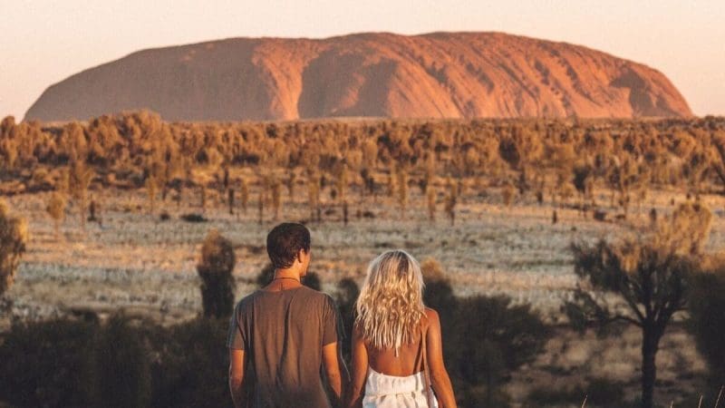 A couple admires Uluru glowing at sunset during a guided 4-day Uluru, Kata Tjuta, Kings Canyon & West MacDonnell desert tour.