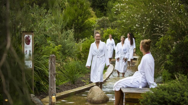 Relaxing at Peninsula Hot Springs: five women in white robes enjoy a luxury footbath and spa entry via 1 Day Shuttle Bus.