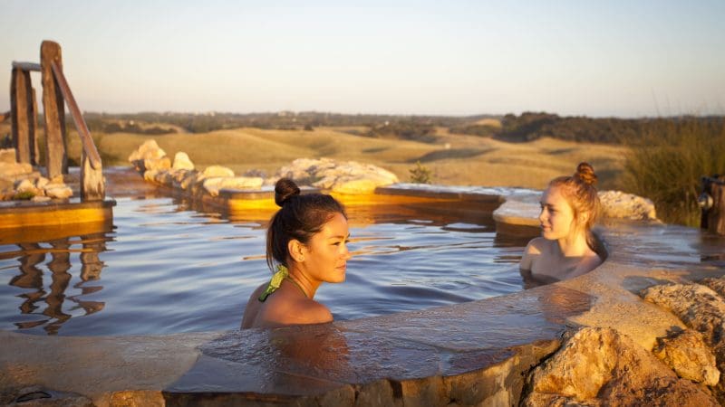 Two women unwind in a scenic hot spring pool at sunset, experiencing 1 Day Peninsula Hot Springs Spa Entry Coach relaxation.