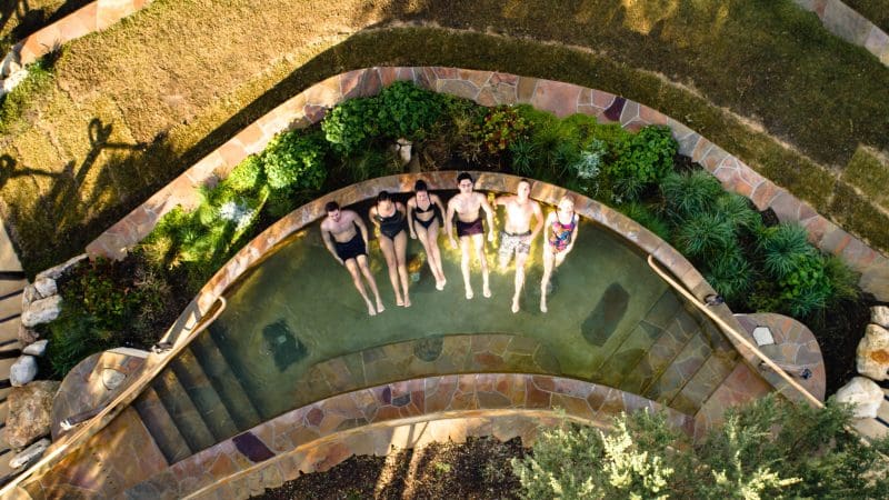 A group of six people in swimsuits unwind together at Peninsula Hot Springs, making the most of a 1 Day Spa Entry with Shuttle Bus.