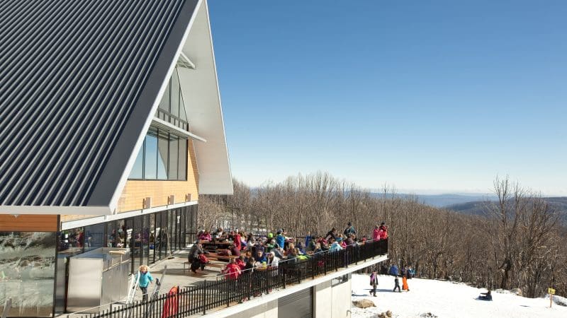 Group of skiers relaxing on a sunlit lodge terrace during a top-rated 1 Day Lake Mountain Snow Waterfalls Tour from Melbourne.
