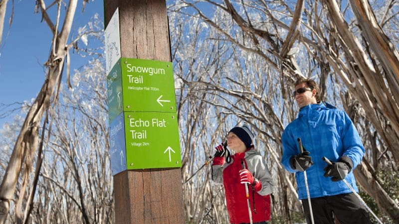 Two travellers in winter gear study trail signs on the snowy Lake Mountain Snow Waterfalls day tour departing from Melbourne.