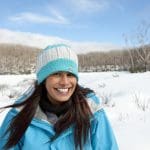 Happy woman in blue jacket enjoying a 1 Day Lake Mountain Snow Waterfalls Tour from Melbourne, with scenic snowy trees behind her.