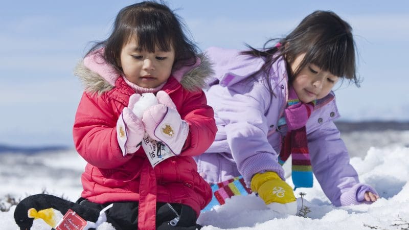 Children in colourful winter coats play joyfully in fresh snow, capturing the fun of a Lake Mountain Snow Tour near Melbourne.