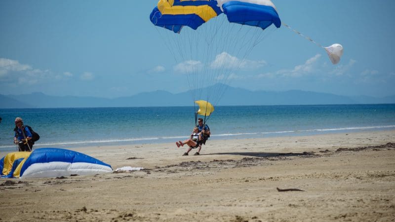 Parasailer lands on Mission Beach; vibrant blue sea, distant mountains, and breathtaking 15,000ft tandem skydive coastal views.