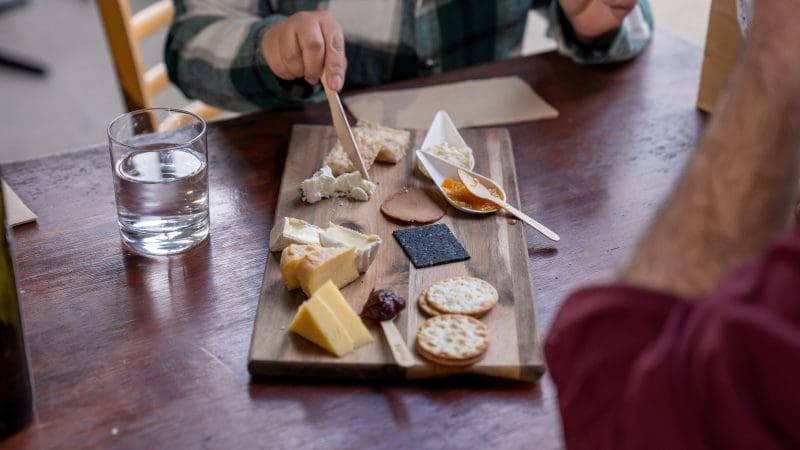 Two guests savour a gourmet cheese board with crackers, spreads, and water on a luxurious Hunter Valley 1 Day Wine Tour experience.