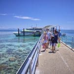 Travellers stroll along a scenic pier above crystal-clear blue waters under the sun, departing for Green Island’s 9am Half-Day Tour.
