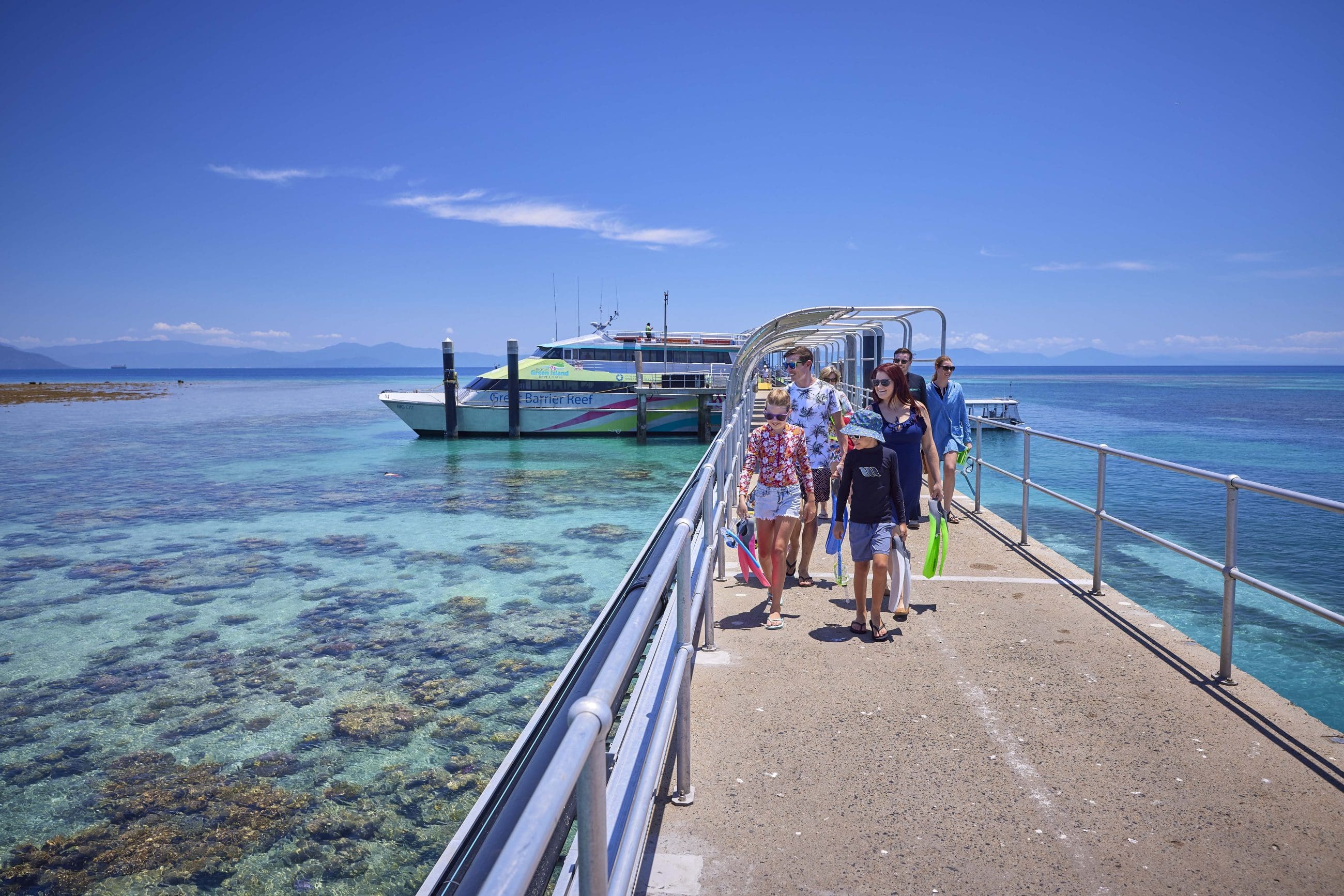 Travellers stroll along a scenic pier above crystal-clear blue waters under the sun, departing for Green Island’s 9am Half-Day Tour.