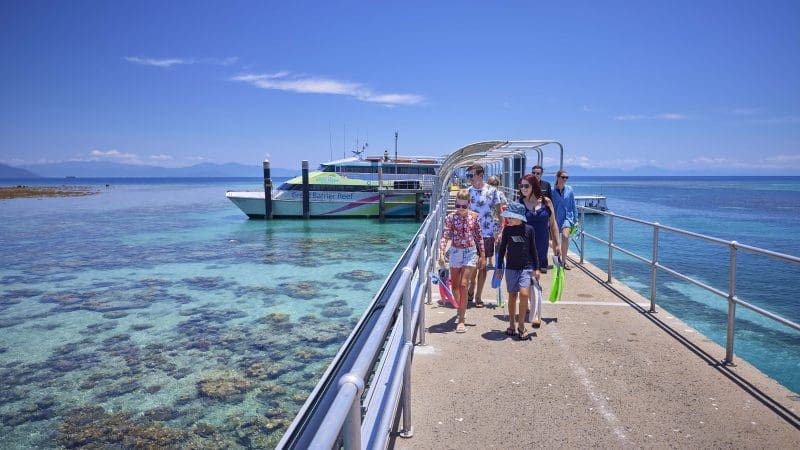 Travellers stroll along a scenic pier above crystal-clear blue waters under the sun, departing for Green Island’s 9am Half-Day Tour.