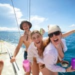 Three friends smiling on a sailboat during their 28 Day Oz East Coast Adventure, enjoying drinks and stunning ocean views in the background.