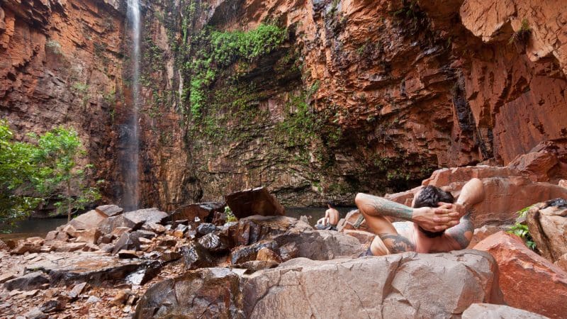 Traveller unwinds on scenic rocks by a cascading waterfall during the 10 Day Broome to Darwin 4WD Kimberley Adventure tour.