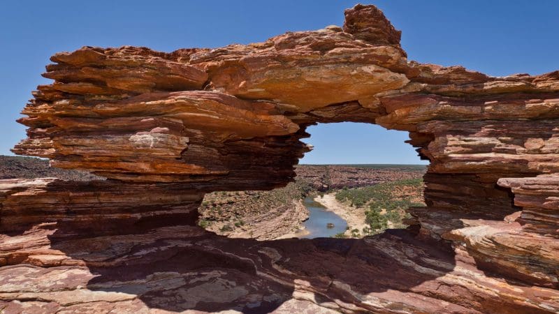 Dramatic natural rock arch overlooking winding river and rugged terrain on 10 Day Broome to Perth West Coast Adventure tour.