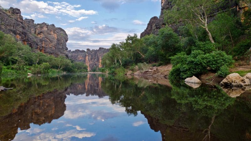 Experience a tranquil river mirroring rugged cliffs and lush trees—iconic landscape on a 10 Day Darwin to Broome 4WD Adventure tour.