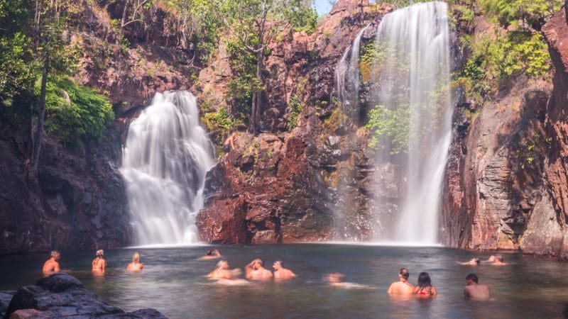 Families enjoying a swim in a stunning natural pool under cascading waterfalls on a Kakadu, Katherine, and Litchfield tour in Australia.