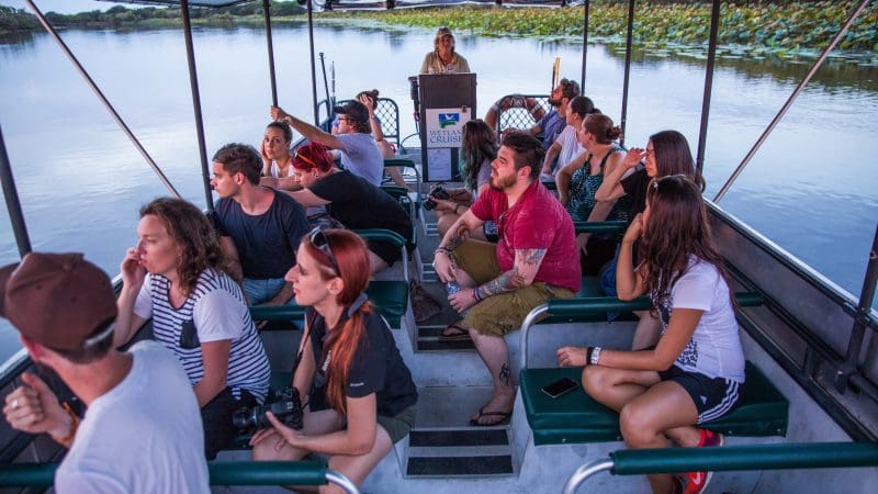 Families on a Kakadu, Katherine, and Litchfield tour listen to an expert guide beside tranquil waters and lush, vibrant Australian scenery.