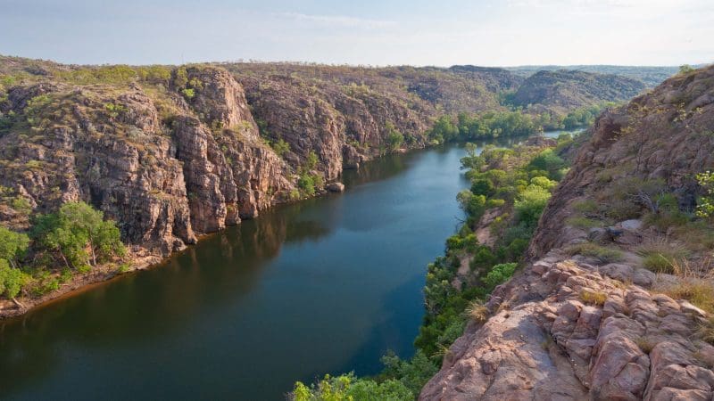 Embark on a Kakadu 4WD adventure: discover a winding river, striking rocky cliffs, and lush greenery beneath dramatic clouded skies.