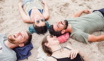 A cheerful group relaxes and plays on the sandy beach during their Grand Kiwi Experience tour in New Zealand.