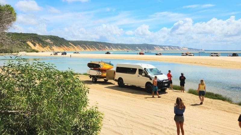Group of people with surf vans on Noosa’s sandy beach, taking surf lessons by the ocean under a vibrant blue, sunny sky.