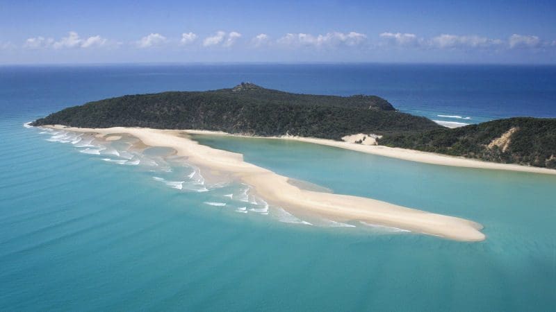 Stunning sandbar arcs through crystal-clear turquoise waters by a vibrant green island, ideal for scenic Noosa beach kayak tours.