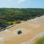 Blue bus parked on sandy beach with lush green forest and ocean waves—ideal for a top-rated Kgari 2 Day Tour from Hervey Bay.