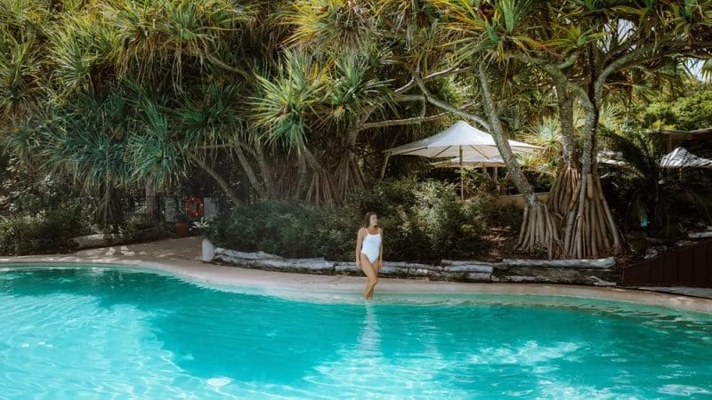 Woman in white swimming costume stands by luxury pool, surrounded by lush tropical greenery on Kgari 5 Day Ultimate Escape holiday.