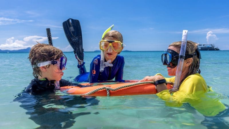 Children snorkelling in crystal-clear blue waters with an orange float ring on a Frankland Island Express Tour, Great Barrier Reef.