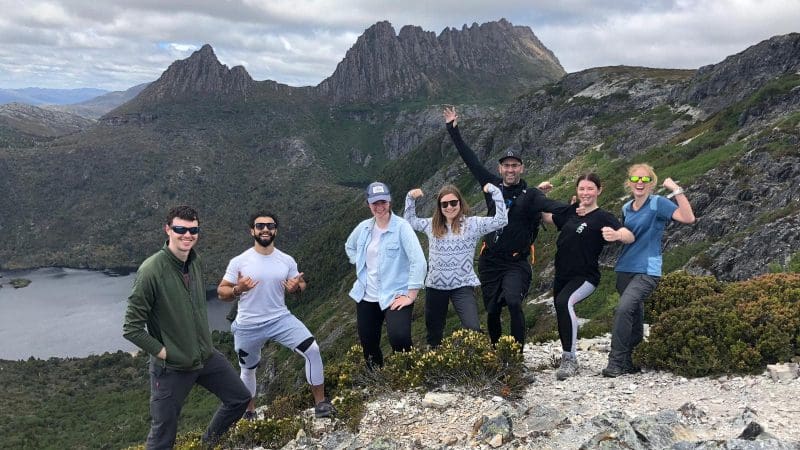 Seven adventurers beam with excitement atop a rugged Cradle Mountain trail on a 2 Day Hobart tour with Wild Tasmania Tours.