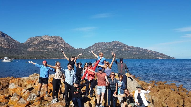 Adventurers smiling on rugged coastal rocks during the 4-Day Wild Tasmania Wilderness Loop, guided by Wild Tasmania Tours.