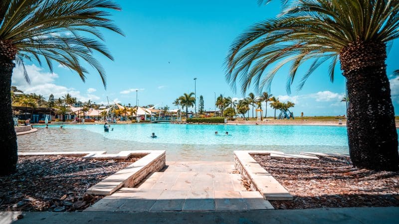 Spacious swimming pool with active swimmers, palm trees, and tropical-style resorts—unwind after your fully guided Sydney to Cairns tour.