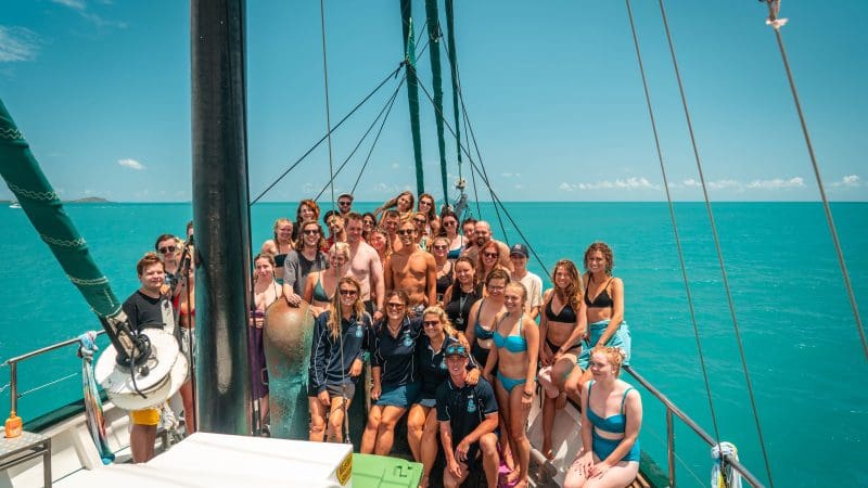 Group of friends in colourful swimwear enjoying a guided sailboat tour on the Ultimate East Coast Sydney to Cairns adventure.