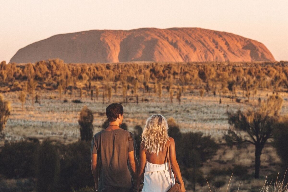 Couple watching sunset over Uluru in the Australian Outback desert during a 2 Day Red Centre Rock Tour from Alice Springs.