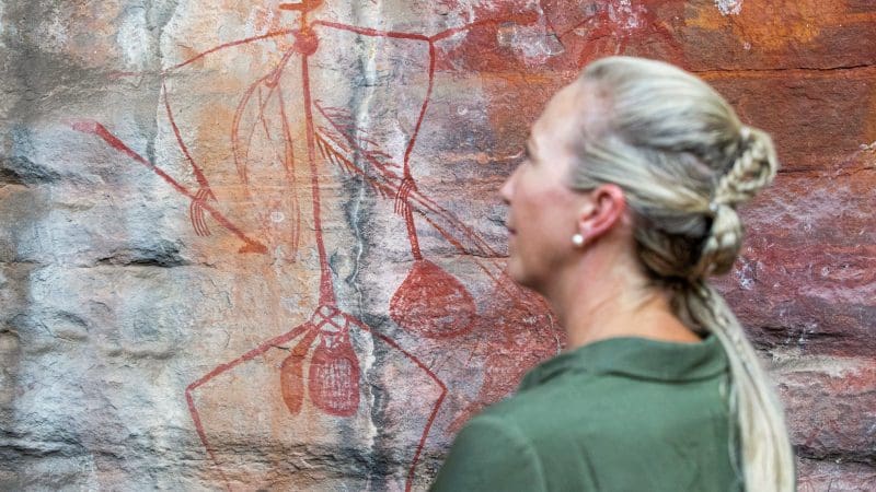 Blonde woman admiring ancient Aboriginal rock art during the 5 Day Kakadu, Katherine Gorge & Litchfield 4WD Adventure in Australia.