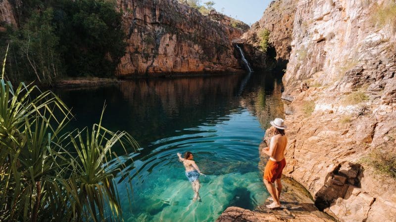 Two adventurers relax at a scenic rocky waterhole on a 5-Day Kakadu, Katherine Gorge & Litchfield 4WD tour from Darwin.