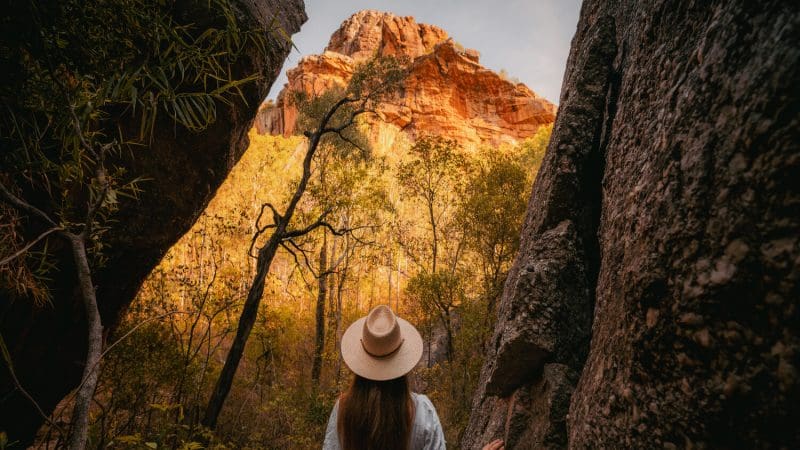 Traveller in wide-brimmed hat stands among rugged rocks, gazing at scenic mountains on a Kakadu, Katherine Gorge, Litchfield 4WD tour.