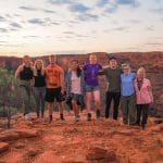 Group of eight adventurers smiling on a rocky sunset cliff during a 7 Day Adelaide to Uluru Untamed Escapes tour experience.