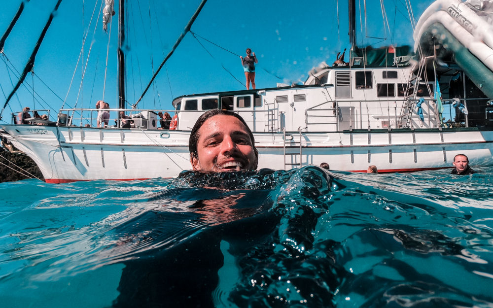 A happy swimmer enjoys crystal-clear Whitsunday waters near New Horizon during a 2 Day 2 Night sailing adventure under sunny skies.