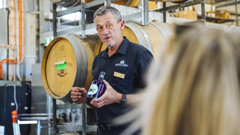 Expert wine tour guide in black shirt showcases premium bottle during Hunter Valley Signature Wine Tour by rustic winery barrels.