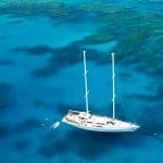 The Summer Jo 2 white sailboat anchored in crystal-clear Whitsunday waters with swimmers exploring vibrant coral reefs below.